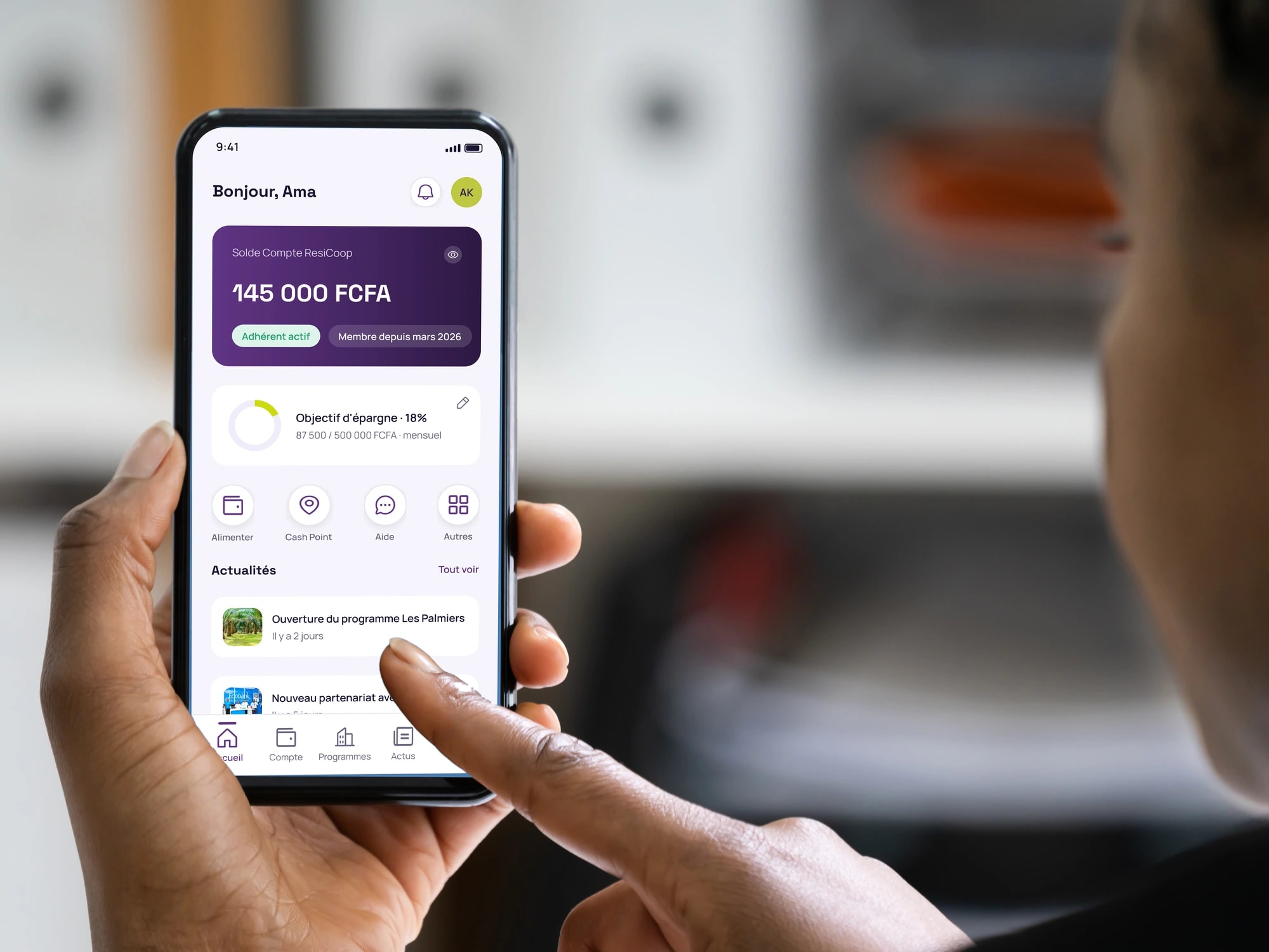 Une main tient un téléphone ouvert sur l'accueil de l'application ResiCoop